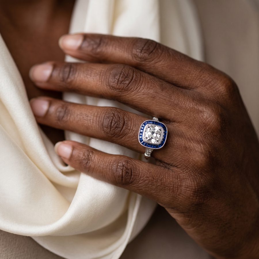 Art deco sapphire and diamond halo ring on a hand against cream silk, AI lifestyle render