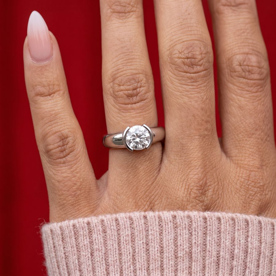 Bezel-set round diamond solitaire ring on a hand against a red background, AI render from a product URL