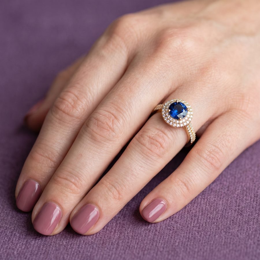 Blue sapphire halo engagement ring with diamond shoulders on a hand, AI lifestyle render