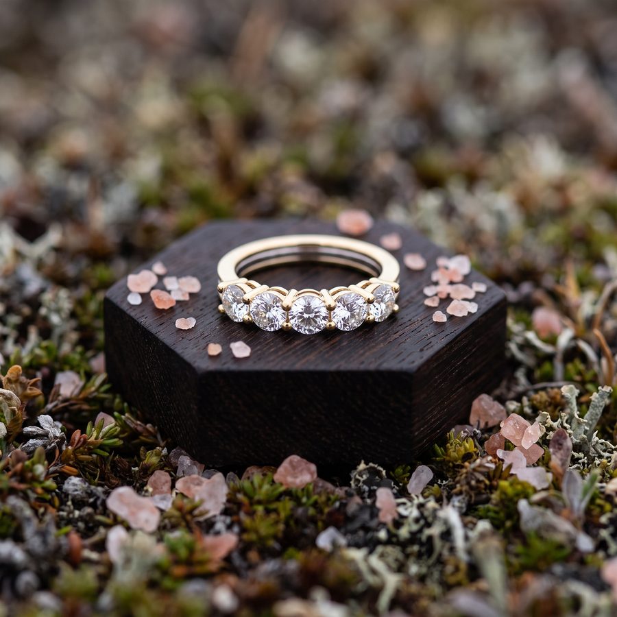 Diamond eternity ring on a dark timber block set in moss and petals, AI lifestyle render