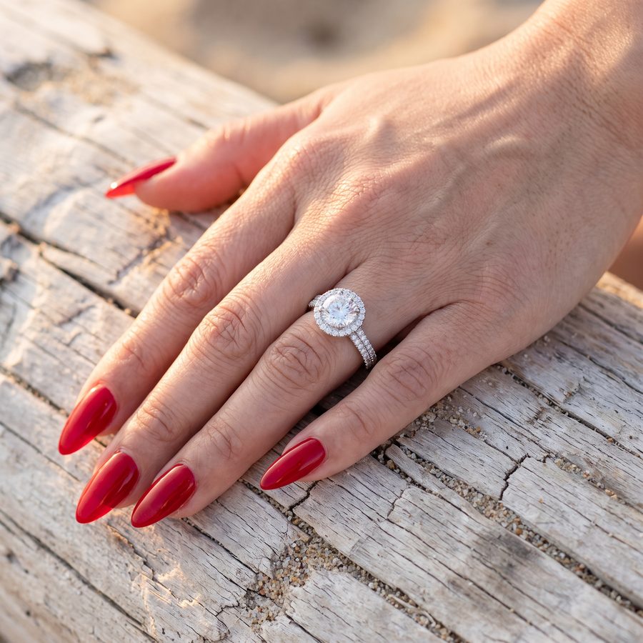 Round diamond halo ring with a pave set band on a hand, AI lifestyle render on weathered wood