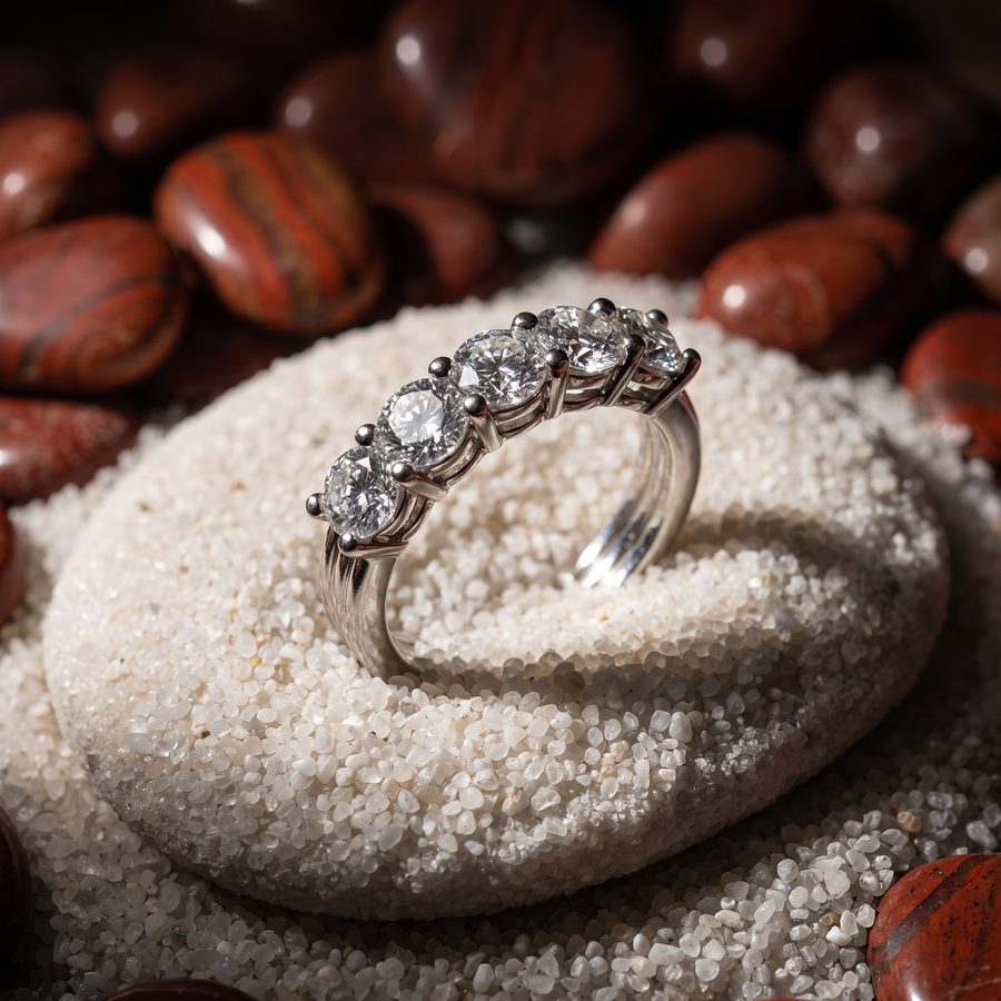 Five stone diamond eternity ring on a pale pebble with red jasper stones, AI studio render