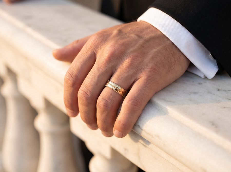 Men's plain yellow gold wedding band on a hand resting on a stone balustrade, AI lifestyle render
